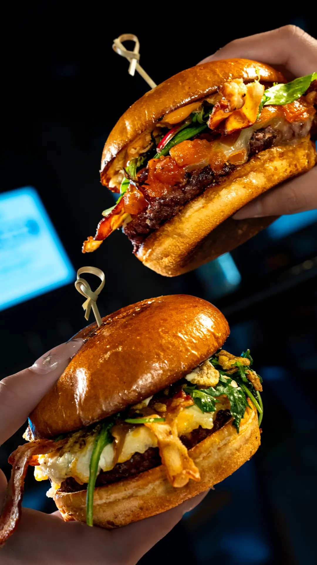 Dos manos sosteniendo hamburguesas con tocino